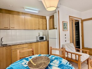 Eine kompakte Küche mit Holzausstattung, einer Mikrowelle, einem Kühlschrank und einem Essbereich mit Tisch und Stühlen.