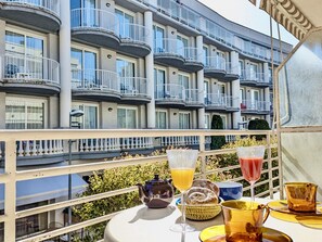 Ein Balkon mit Frühstückstisch, komplett mit Teekanne, Gläsern und Gebäck, mit Blick auf ein mehrstöckiges Gebäude mit Balkonen.