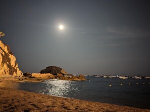 Eine Küstenlandschaft mit felsigem Ufer, einem kleinen Hügel und Booten im Wasser.
