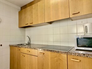 Eine Küche mit Holzschränken, einer Arbeitsplatte aus Granit, einer Edelstahl-Spüle und einer Mikrowelle.