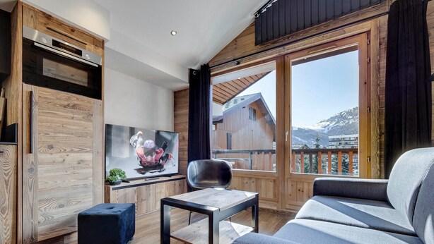 Een moderne woonkamer met houten details, een televisie, een bank, een tafel en uitzicht op een berglandschap.