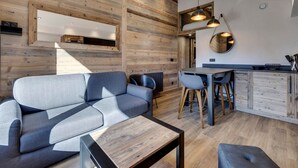 Een modern interieur met een houten wand, een bank, een eettafel met stoelen en hanglampen.