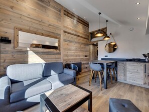 A modern interior with a wooden wall, a sofa, a dining table with chairs, and pendant lighting. - Renovated apartment in Val-d'Isère - 4 guests (Val-d'Isère)
