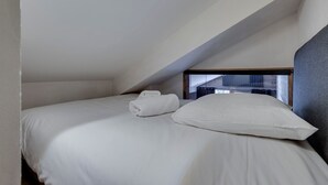 Een eenpersoonsbed in een kamer met een schuine plafond, wit beddengoed en een zichtbaar raam.