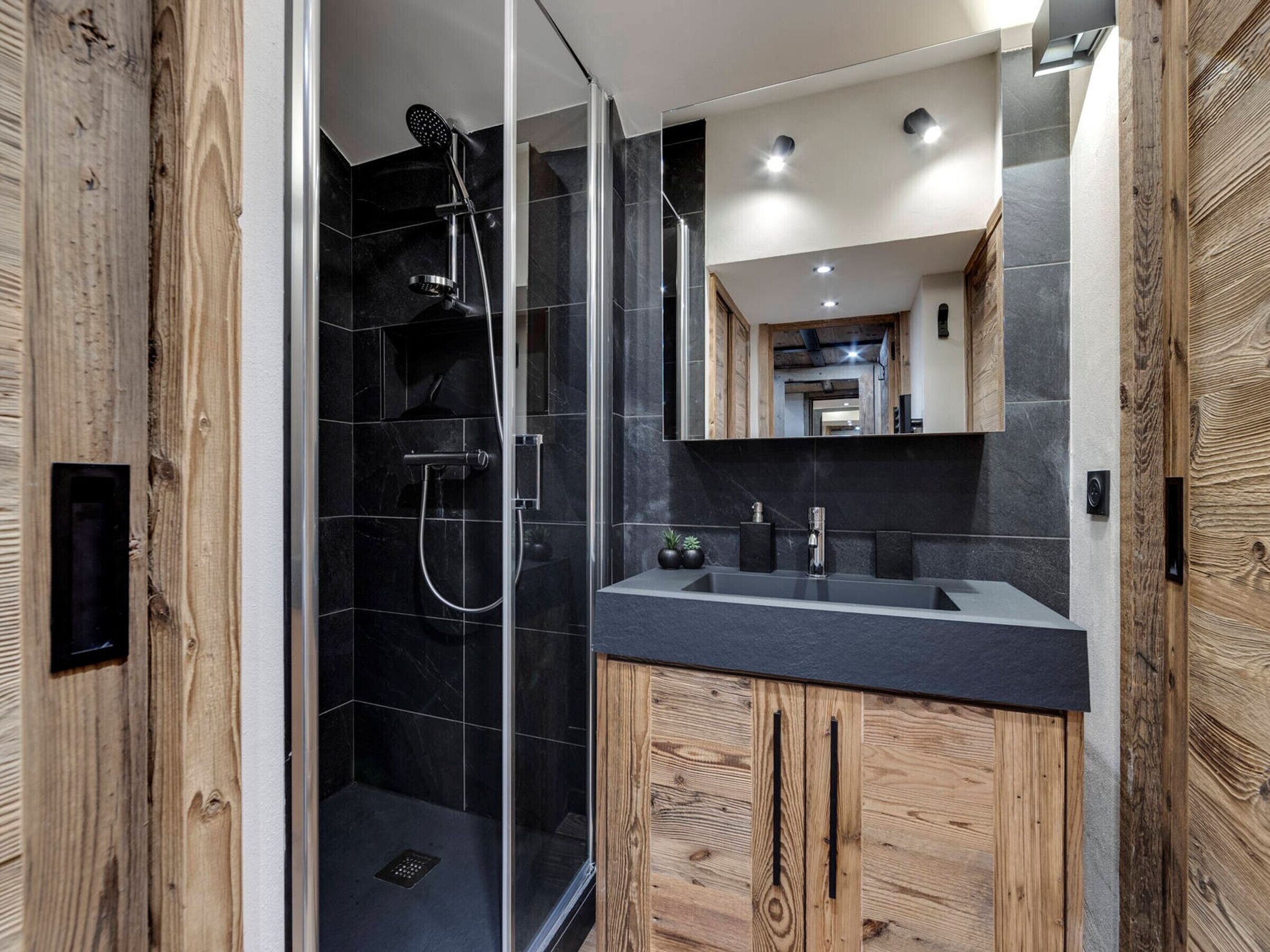 Un baño moderno con ducha envuelta en vidrio, tocador de madera y un espejo grande.