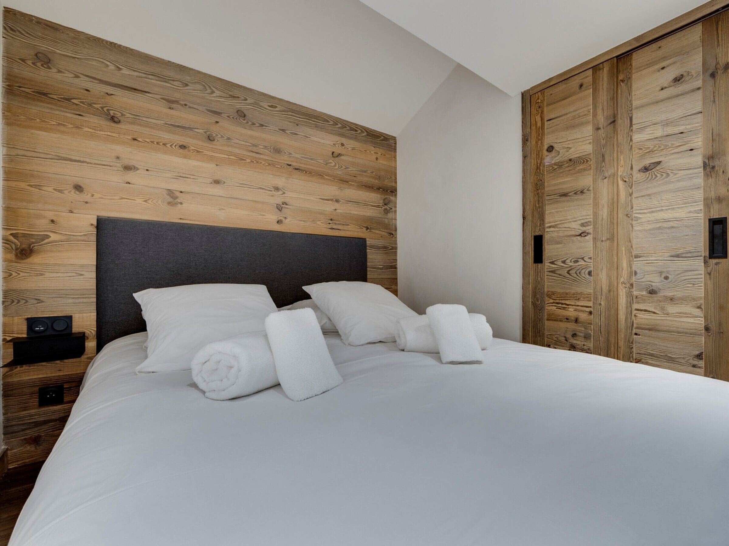 A bedroom with a wooden headboard, a bed with white linens, and a wooden wardrobe.
