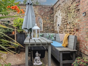 A wooden bench with cushions, a lantern, and a Buddha statue in a garden area with plants and a stone wall. - Old Cottages: 1 Bed Apartment (Ripon)