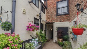 A narrow alleyway with hanging flower baskets and potted plants. - No 1 Old Cottages (Ripon)