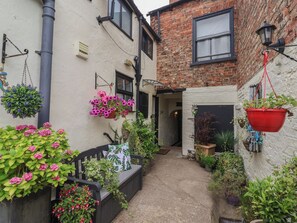 A narrow alleyway with hanging flower baskets and potted plants. - No 1 Old Cottages (Ripon)