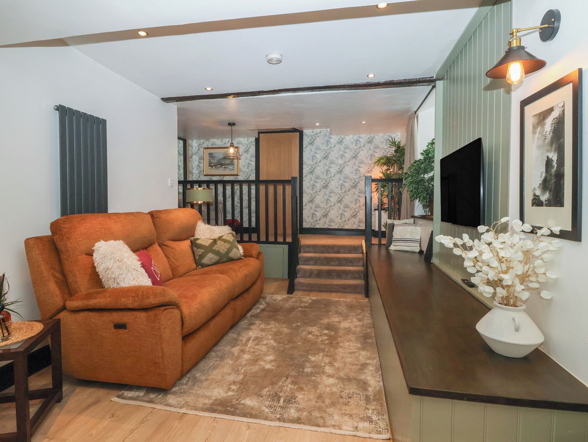 A living room with a sofa, a coffee table, a rug, a staircase, and a TV.