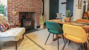 A cozy living room with a brick fireplace, a dining area with a wooden table and chairs, and a comfortable sofa. - No 1 Old Cottages (Ripon)