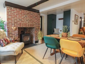A cozy living room with a brick fireplace, a dining area with a wooden table and chairs, and a comfortable sofa. - No 1 Old Cottages (Ripon)