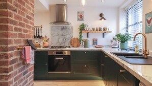 A kitchen with a marble island, stainless steel appliances, and a brick wall. - No 1 Old Cottages (Ripon)