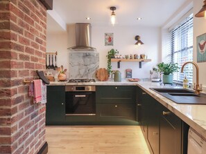 A kitchen with a marble island, stainless steel appliances, and a brick wall. - No 1 Old Cottages (Ripon)