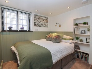A bedroom with a bed, a window with blinds, a wall-mounted shelf with decorative items, and a wall art piece. - No 1 Old Cottages (Ripon)