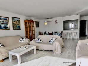 A living room with a sofa set, a coffee table, a wooden cabinet, and a kitchen area with a bar. - Seafront apartment, pets - 6 guests (Tossa de Mar)