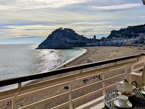 A beach with a rocky outcrop, a clear sky, and buildings in the background. - Seafront apartment, pets - 6 guests (Tossa de Mar)