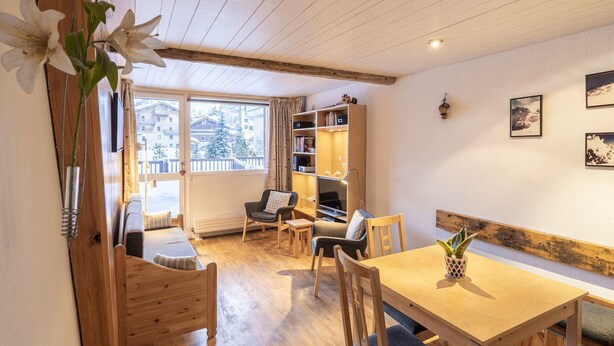 A cozy room with a wooden ceiling, a dining table with chairs, a bookshelf, and a window with a view of buildings. - Family apartment in center, mountain view - 4 guests (Val-d'Isère)