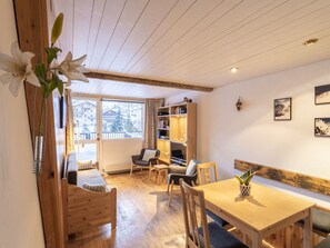 A cozy room with a wooden ceiling, a dining table with chairs, a bookshelf, and a window with a view of buildings. - Family apartment in center, mountain view - 4 guests (Val-d'Isère)
