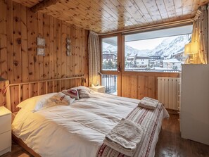Ein Schlafzimmer einer Holzhütte mit einem Bett, Nachttischen, einem Fenster mit Blick auf schneebedeckte Berge und einer Heizung.