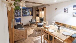 A dining area with wooden furniture, a table set for two, and a bookshelf in the background. - Family apartment in center, mountain view - 4 guests (Val-d'Isère)