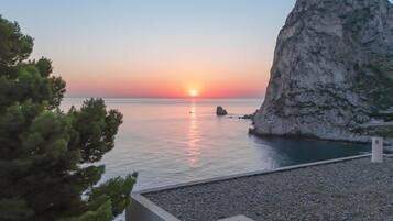 A sunset over a calm sea with a rocky outcrop on the right.
