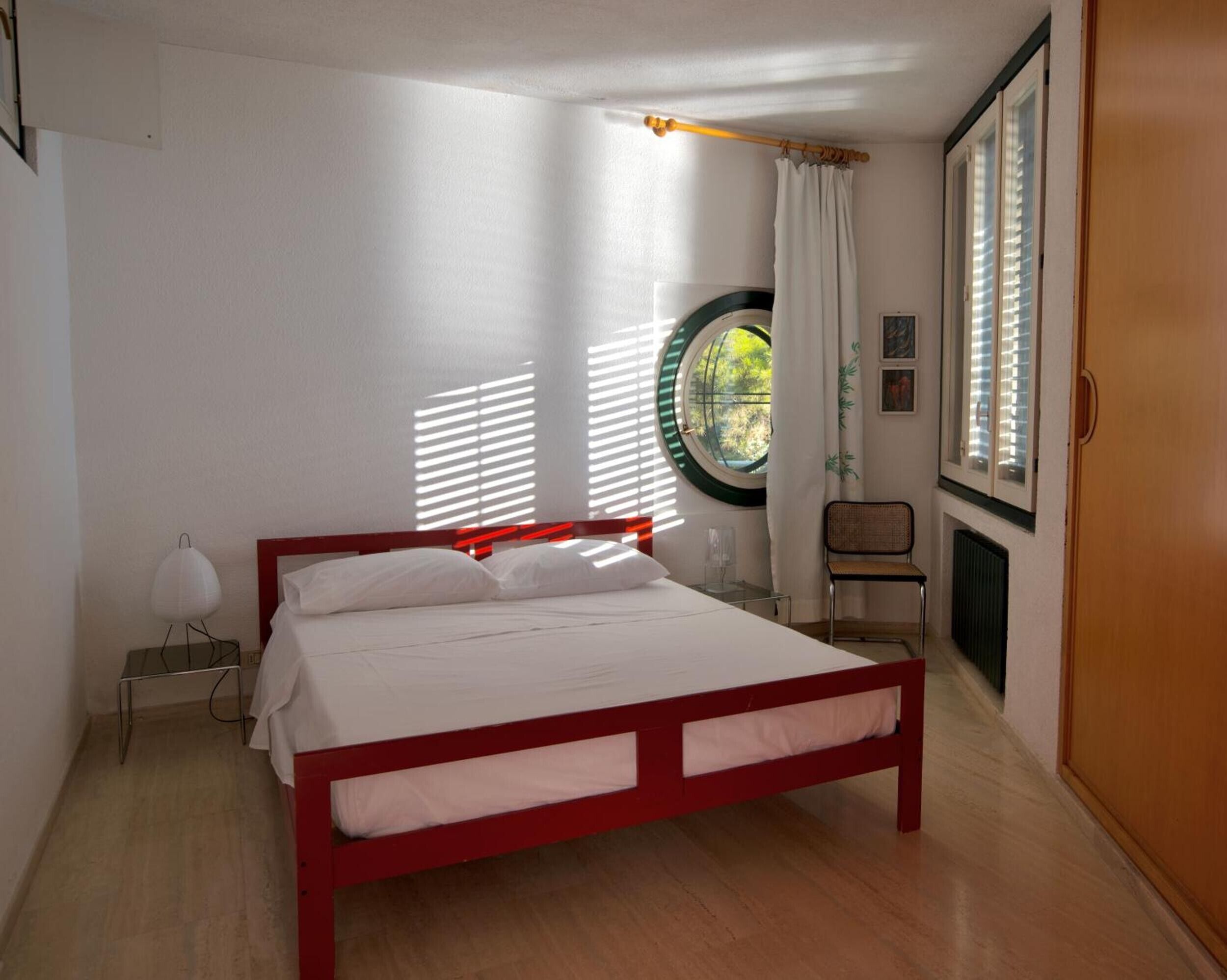 A bedroom with a bed, a window with blinds, a chair, and a radiator.