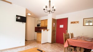 A compact living space with a dining area, kitchenette, and a television mounted on the wall. - Spacious apartment, parking - 6 guests (Lanslevillard)