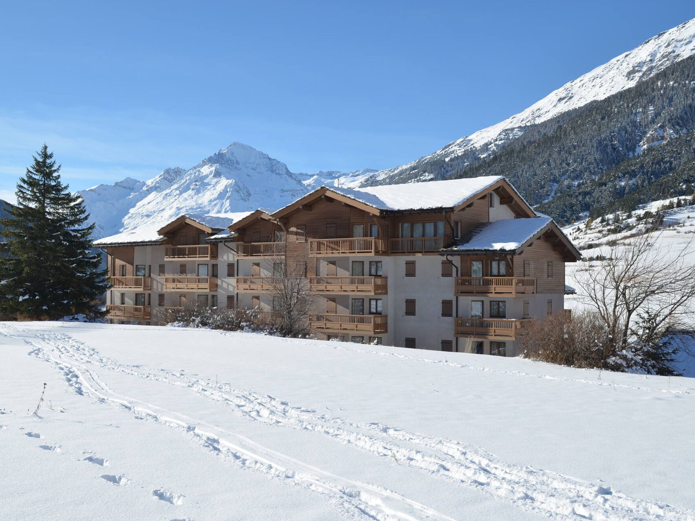 Eine mehrstöckige Holzlodge mit Balkonen vor einer verschneiten Berglandschaft.