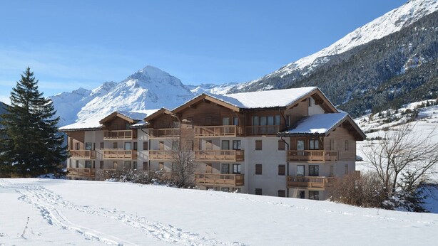 A multi-story wooden lodge with balconies, set against a snowy mountain backdrop. - Spacious apartment, parking - 6 guests (Lanslevillard)