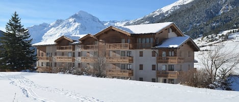 A multi-story wooden lodge with balconies, set against a snowy mountain backdrop.