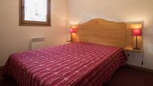 A bedroom with a wooden headboard, two bedside lamps, a window, and a radiator. - Spacious apartment, parking - 6 guests (Lanslevillard)