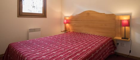 A bedroom with a wooden headboard, two bedside lamps, a window, and a radiator.