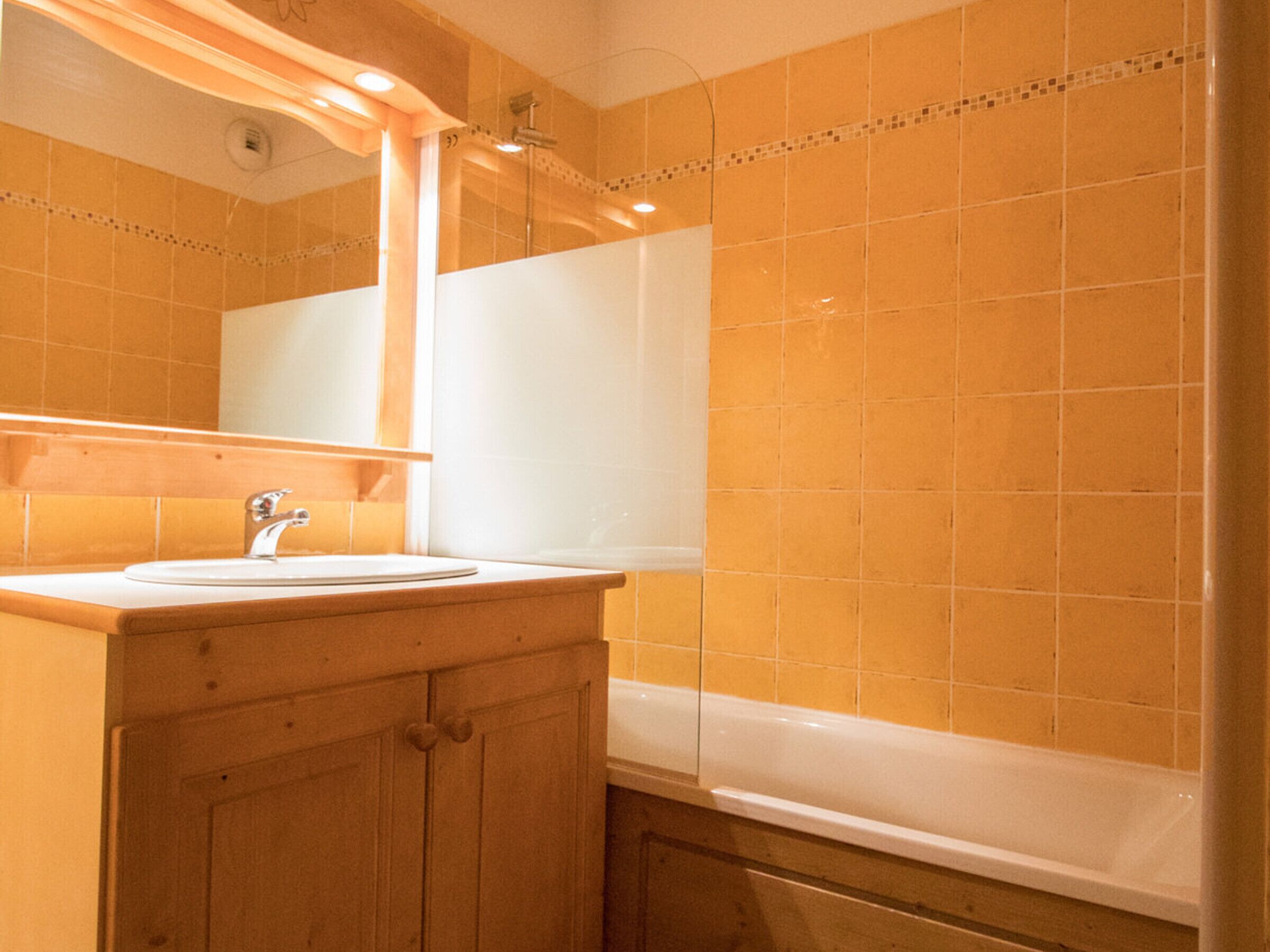 A bathroom with a white sink, wooden vanity, and a bathtub.