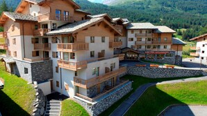 A multi-story hotel with balconies, a stone facade, and a mountain backdrop. - Spacious apartment, parking - 6 guests (Lanslevillard)