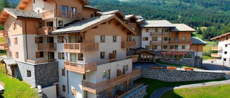 A multi-story hotel with balconies, a stone facade, and a mountain backdrop.