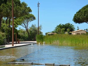 Ein ruhiger Außenbereich mit Wasserspiel, umgeben von Bäumen und einem Gebäude im Hintergrund.