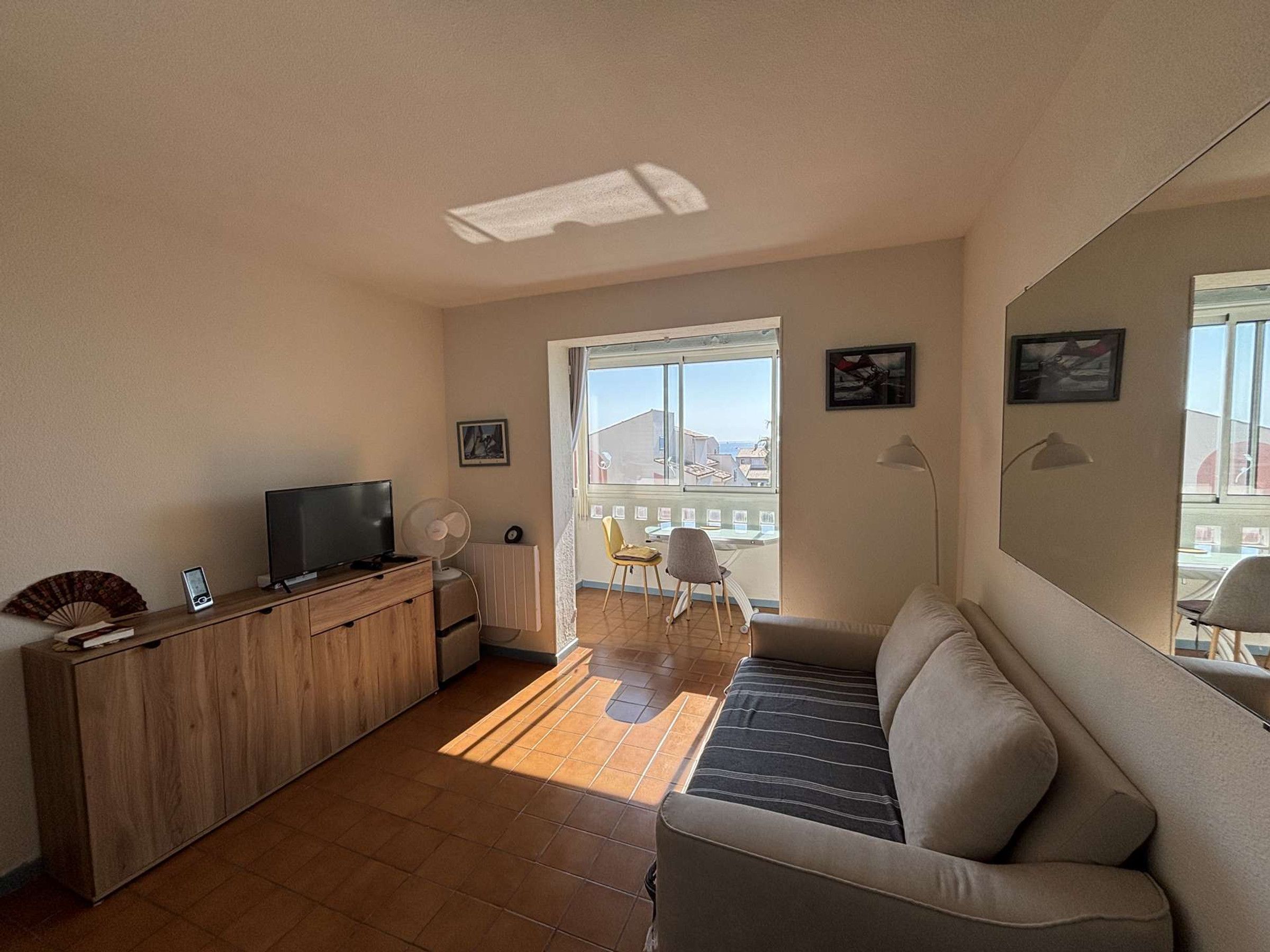 Een woonkamer met een bank, een televisie, een ventilator en een raam met uitzicht.