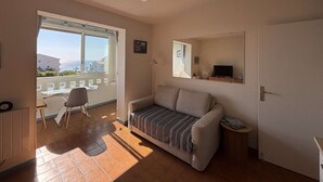 Un soggiorno con divano, un tavolino, una poltrona, televisione e una finestra vista edifici.