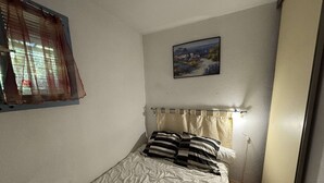 Una camera da letto con un letto singolo, una finestra con tende, un quadro al muro e una lampada da comodino.