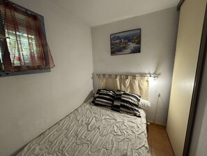 Ein Schlafzimmer mit einem Einzelbett, einem Fenster mit Vorhängen, einem Bild an der Wand und einer Nachttischlampe.