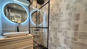 Une salle de bain moderne avec une douche à parois de verre, un miroir rond et un meuble-lavabo en bois.