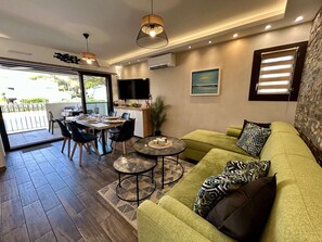 A modern living room with a green sofa, a dining table with chairs, a small coffee table, and a TV mounted on the wall. - Apartment with pool, parking - 6 guests (Cap d'Agde)
