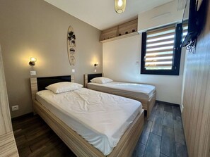 Ein Hotelzimmer mit zwei Betten, einer Surfbrettdarstellung, einem Fenster mit Jalousien und einer an der Wand befestigten Leuchte.