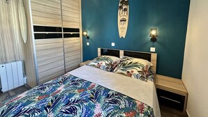 Une chambre à coucher avec un lit, une décoration sur le thème du surf et une fenêtre avec des stores.