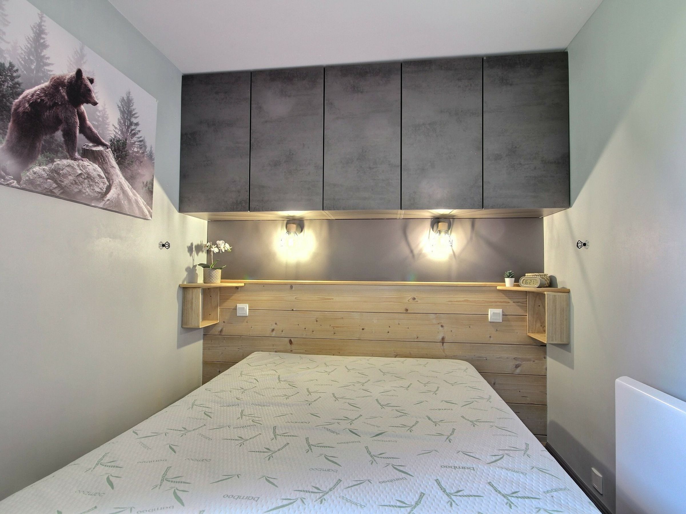 A bedroom with a bed, wooden headboard, wall-mounted shelves, and a bear painting.