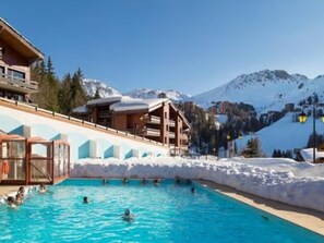 Ein Poolbereich mit Schwimmenden, umgeben von Gebäuden und schneebedeckten Bergen.
