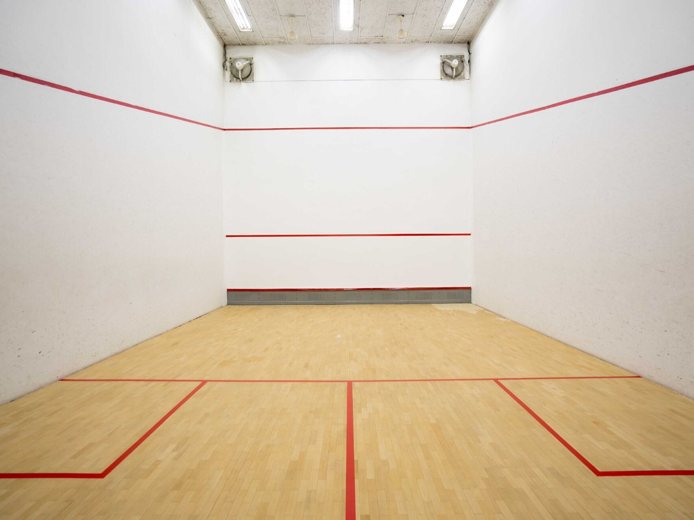 A squash court with wooden flooring and red boundary lines.