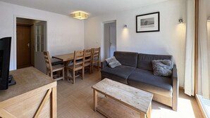 Ein modernes Wohnzimmer mit Sofa, Couchtisch, Esstisch und Stühlen. An der Wand hängt ein gerahmtes Bild, und eine Deckenleuchte erhellt den Raum.
