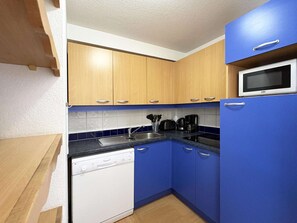 A compact kitchen with wooden cabinets, a dishwasher, a microwave, and a blue countertop. - Ski-in/ski-out apartment - 8 guests (Les Orres)